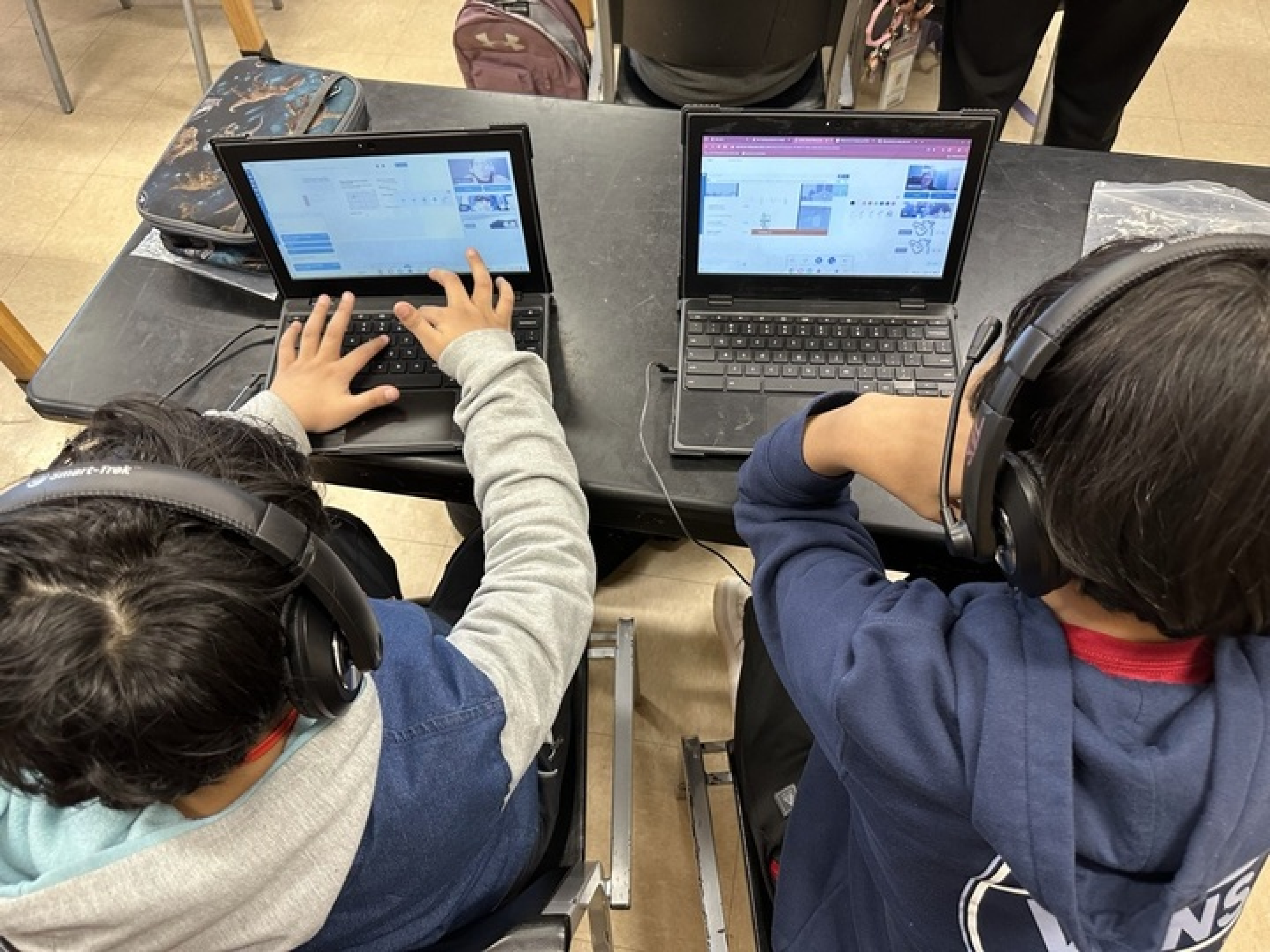 Two elementary students sitting at a desk on laptops being tutored using Littera