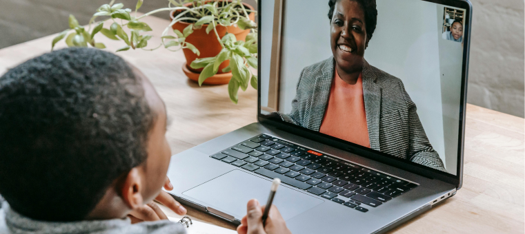 Photo of a medium-dark skinned boy video chatting with a smiling, dark-skinned woman